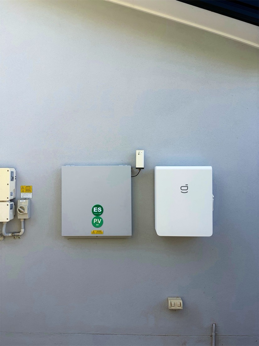 Battery enclosure with energy storage and PV signage next to a white wall-mounted unit
