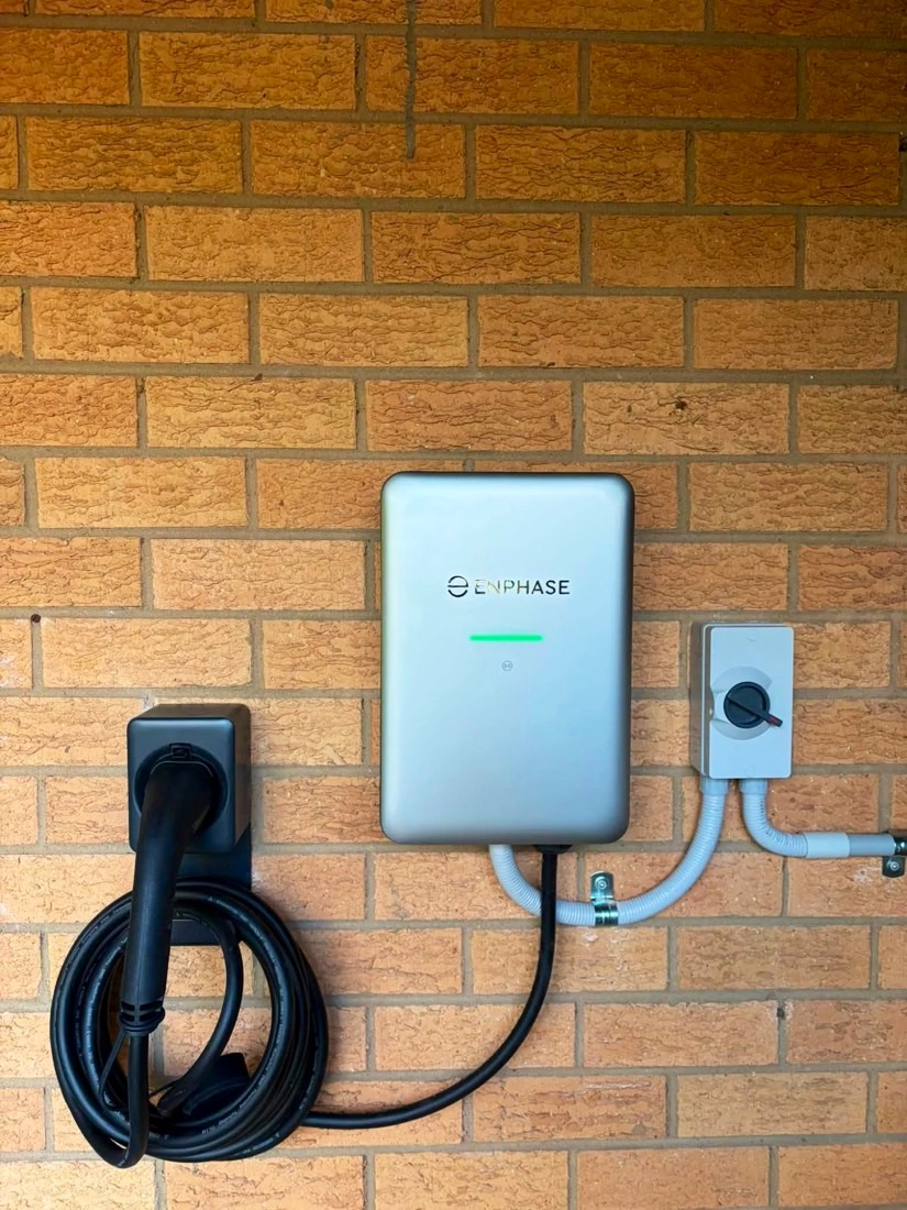 Enphase IQ EV Charger on a brick wall with its cable coiled on a holster and an isolator beside it