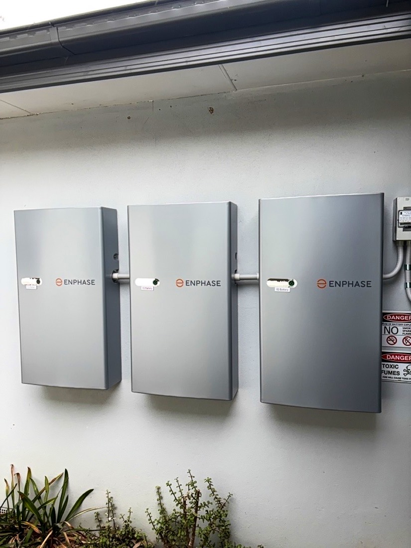 Three Enphase batteries mounted on a rendered wall in Tuggeranong