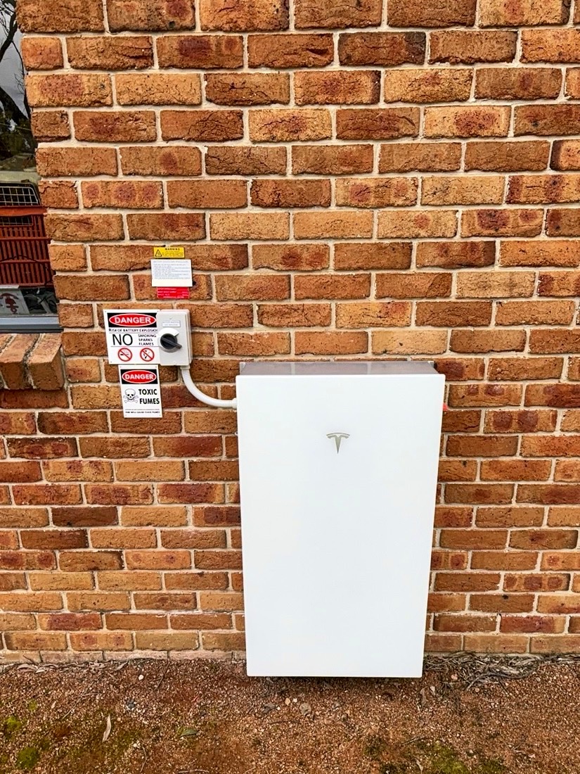 White Tesla Powerwall 3 on a brown brick wall with isolator and signage