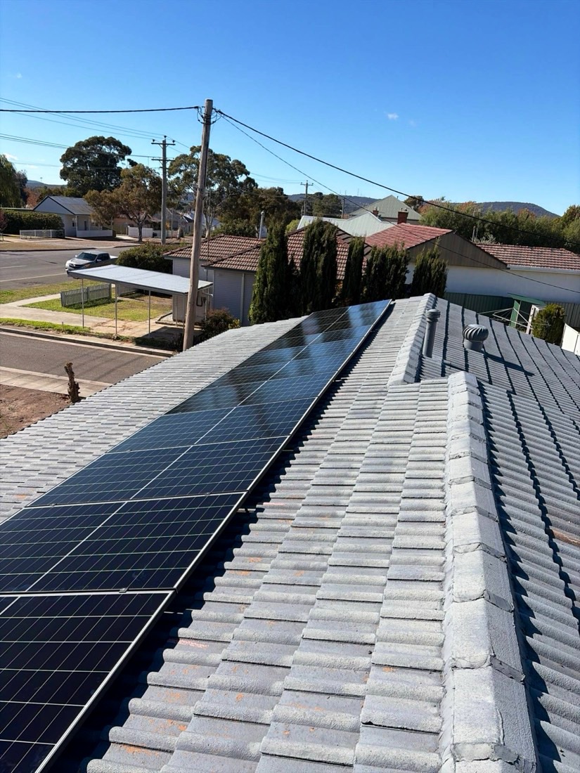Row of black solar panels along a grey concrete tile roof