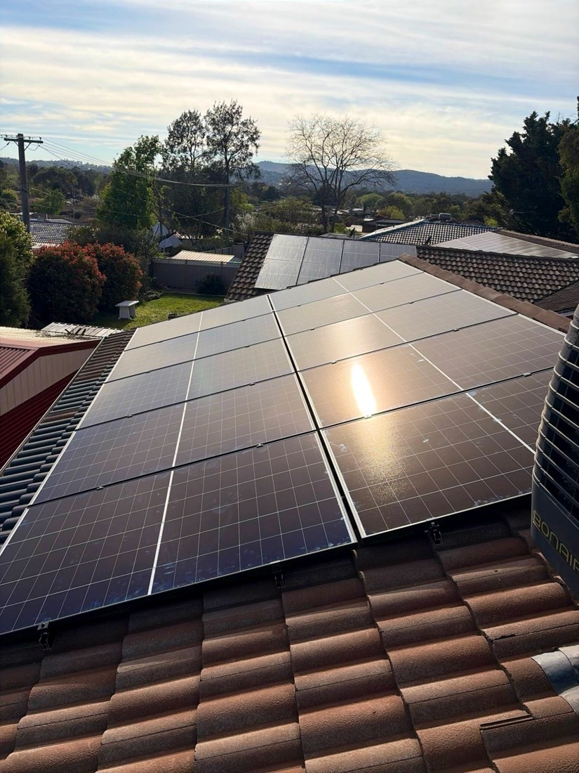 Two rows of black solar panels on a terracotta tile roof catching the late afternoon sun, with hills in the background
