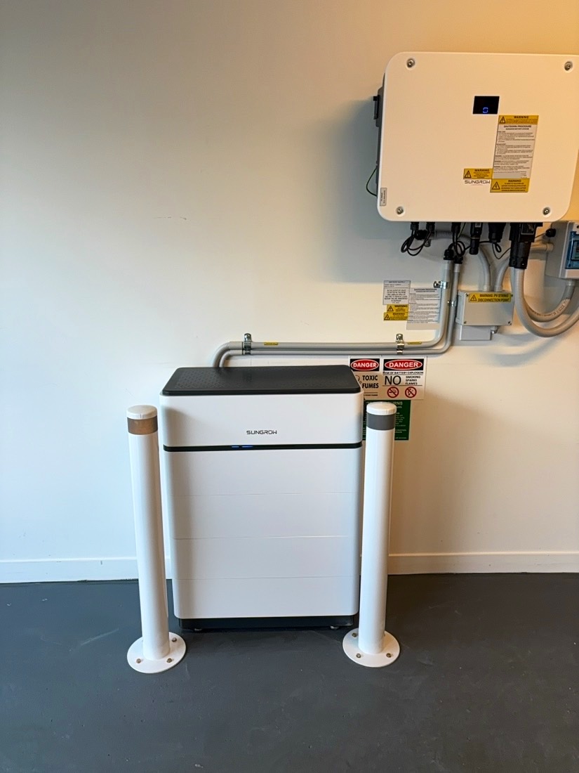 Sungrow battery between two white bollards below a wall-mounted Sungrow inverter