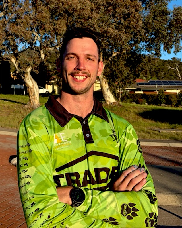 Joey smiling with his arms crossed, wearing a green Advanced Electrical work shirt