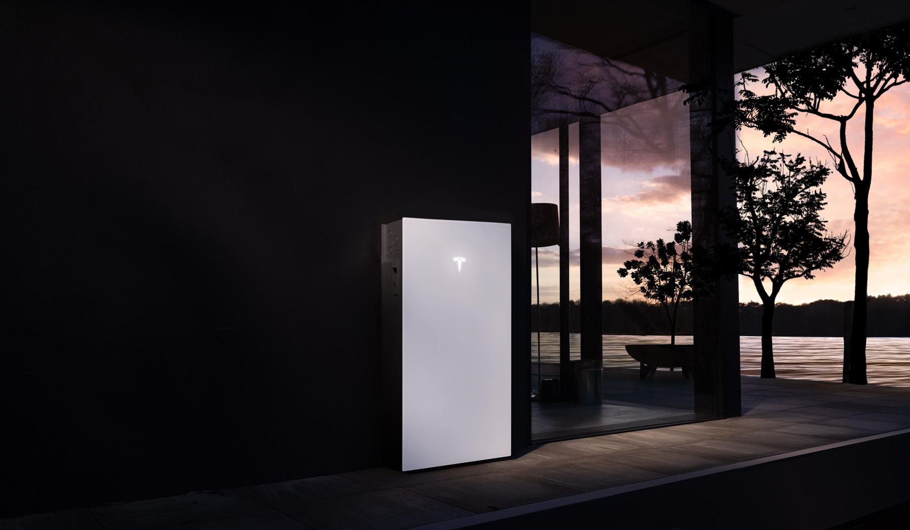 Tesla Powerwall 3 glowing on a dark exterior wall at dusk beside a glass window
